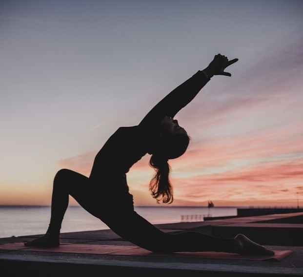 Silhouette of a woman in a yoga low lunge with arms raised on a pier at sunset over the ocean
