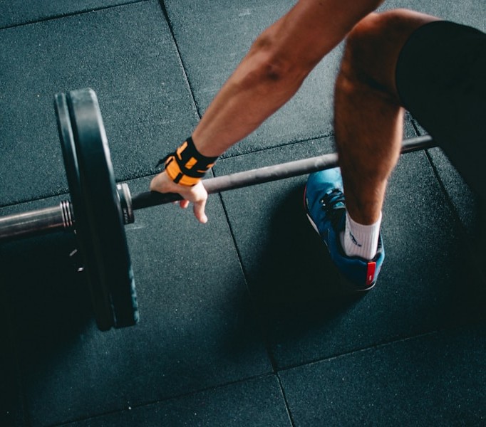 Overhead view of a person gripping a barbell with weight plates on a gym floor mat